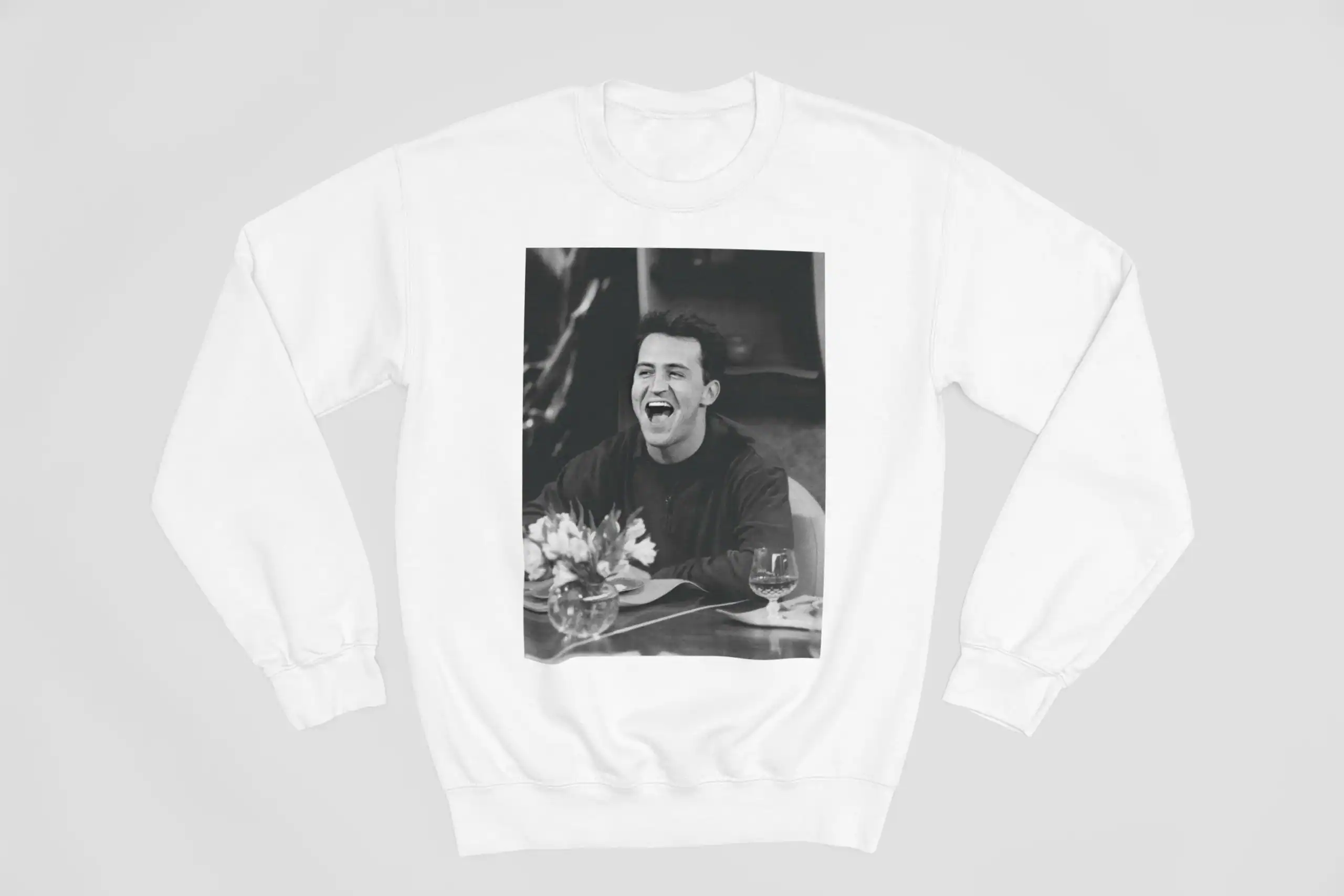 Justin Bieber swag merchandise sweatshirt featuring a black-and-white photo of him laughing while seated at a dinner table with flowers and glasses. Perfect for fans showcasing their Bieber love.