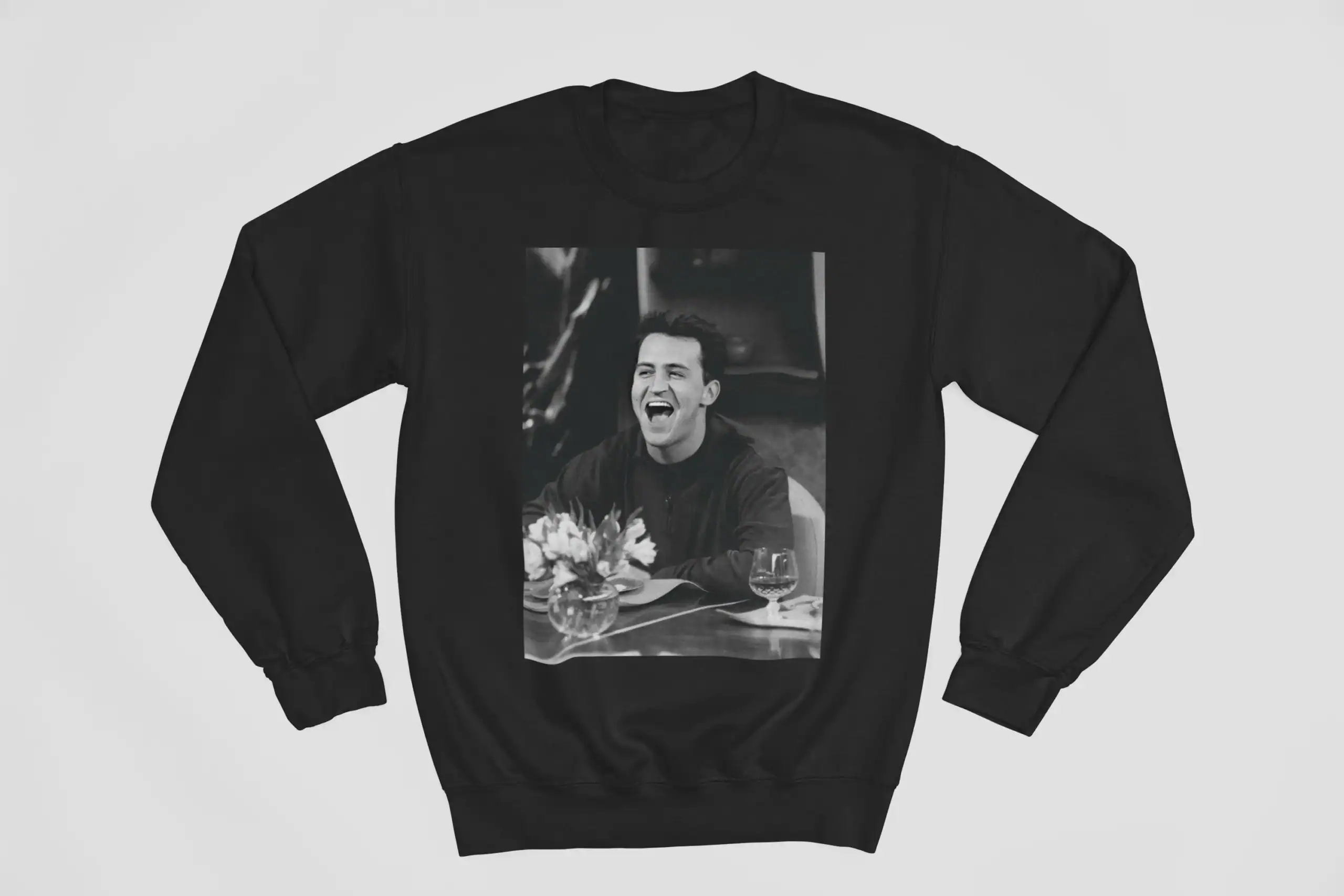 Justin Bieber swag merch sweatshirt featuring a black and white photo of the pop star laughing, sitting at a table with flowers and wine, perfect for fans of his stylish clothing line.